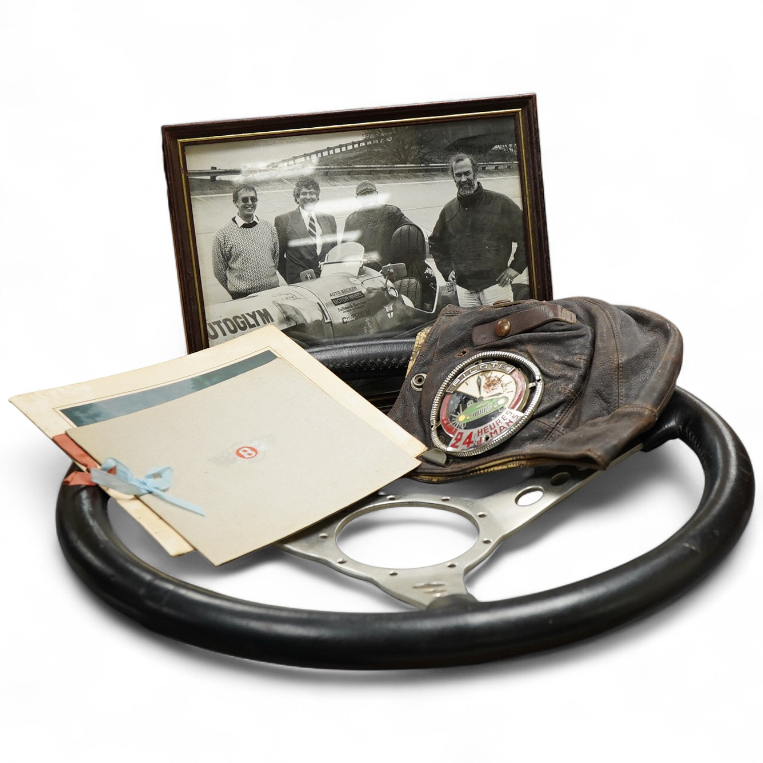 Racing ephemera, including; a Moto-lite steering wheel, a driver's leather cap, an enamelled Le Mans pilot’s radiator badge, signed photograph of Prince Michael Kent standing next to a 12 cylinder single seat racing car